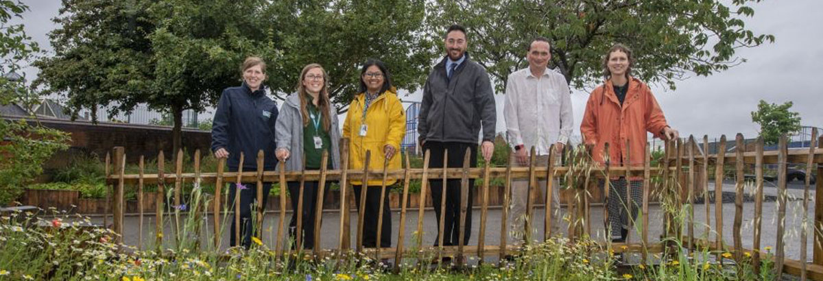 A group of smiling people standing behind a low wooden fence with wild flowers in front