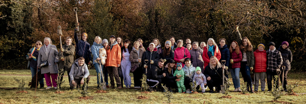 A group of people in a line holding shovels in the air & standing behind newly planted trees